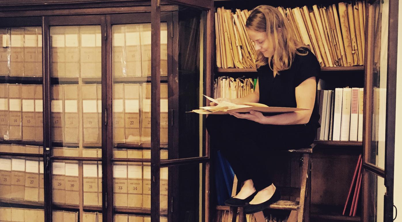 ASLA-Fulbright Graduate Grantee 2016-2017 Petra Kuivala sitting on a ladder in Cuban studies archive room reading a folder