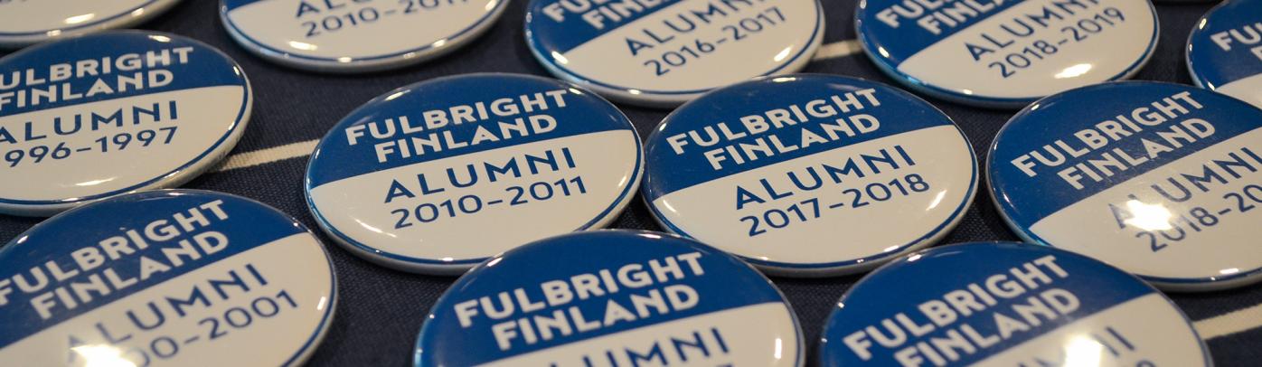 Blue and white buttons saying Fulbright Finland Alumni and a year on a table