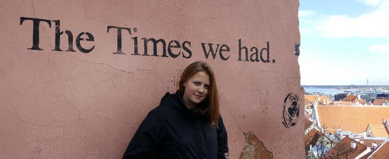 A teenage girl standing in front of a pink wall that has "The Times We Had" written on it. Tallin's old town is visible on the right.