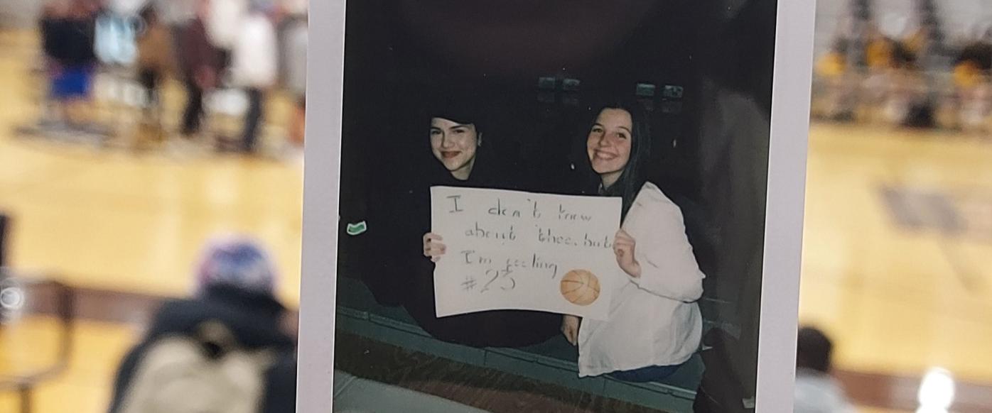 Photo of a polaroid picture where there are two girls holding a sign saying "I don't know about thee, but I'm feeling #23" The photo is taken at a basketball court's seats