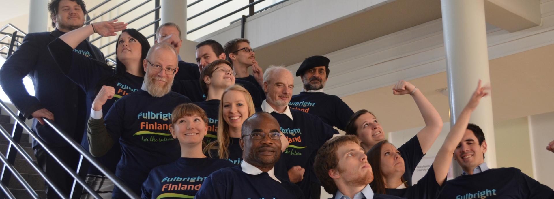 Group of American Fulbrighters wearing Fulbright Finland t-shirts on a staircase making superhero-like moves