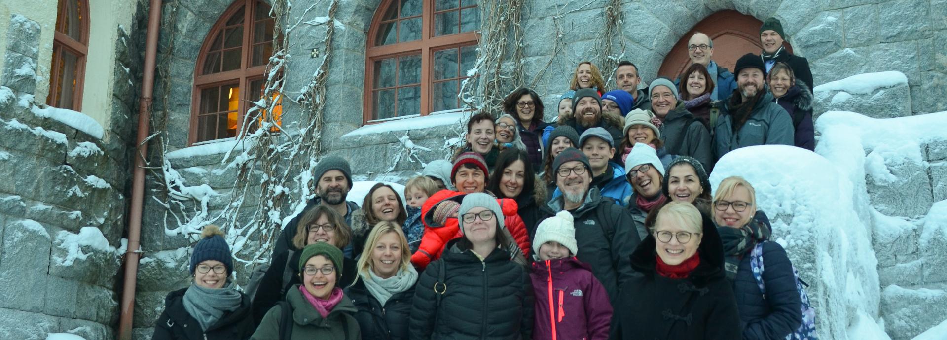 Group of smiling U.S. Grantees on the stairs of the historical Villa Hvittorp. Everyone is wearing winter clothes, as it's January and there is a lot of snow.