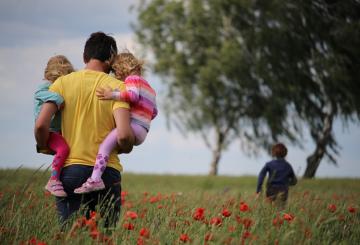 A man carrying two girls on a field of flowers