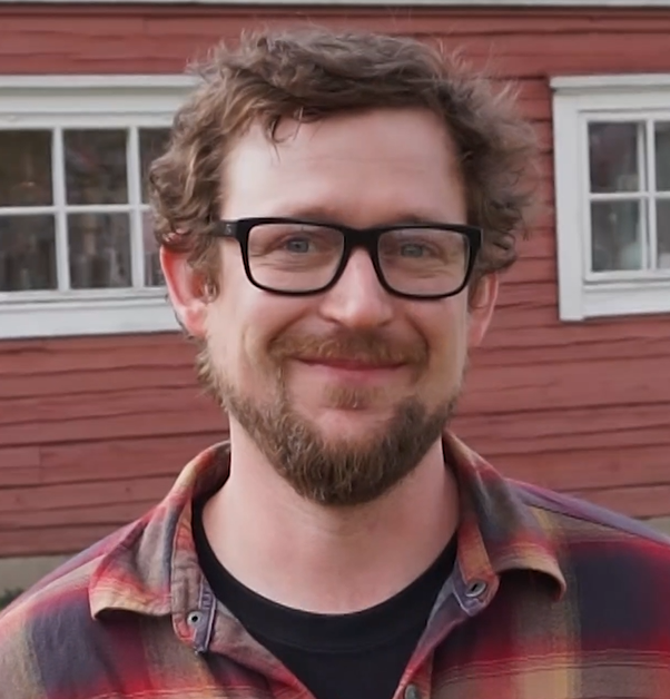 2018-2019 U.S. Fulbright Fellow Jonathan Capps smiling in front of a red wooden house