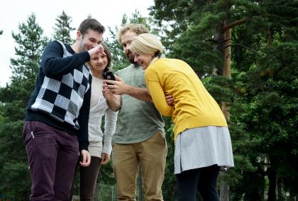 Group of American Fulbright Finland grantees looking a phone in front of pine trees