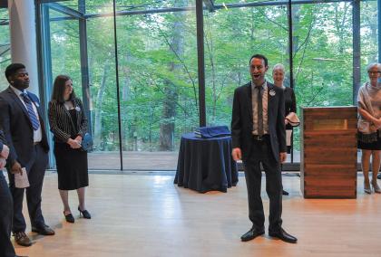 Simon Barrad singing at the Finnish Embassy in Washington D.C. There is a green forest in the background and people listening around Simon