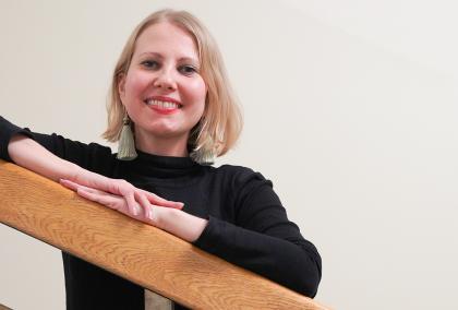 Journalist Kaarina Huovinen slightly leaning on a staircase bannister and smiling to the camera.