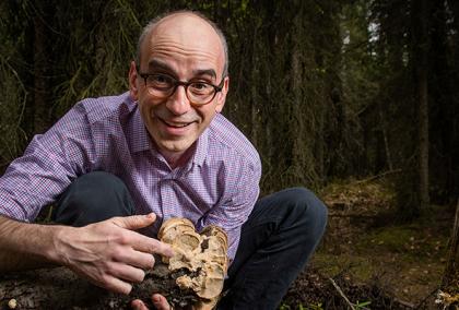 Philippe Amstislavski in a forest, pointing at fungi growing on a tree trunk and smiling at the camera