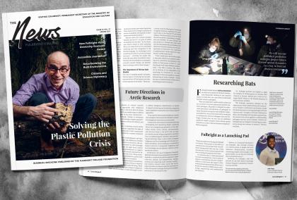 The cover and one spread of the Fulbright Finland News magazine on a greyish background. The cover features U.S. Fulbright scholar Philippe Amstislavski in a forest, and the spread shows article with title "Researching Bats" and "Fulbright as a Launching Pad".
