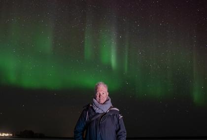 Michael West standing in the middle of the photo with green and red aurora borealis behind him.