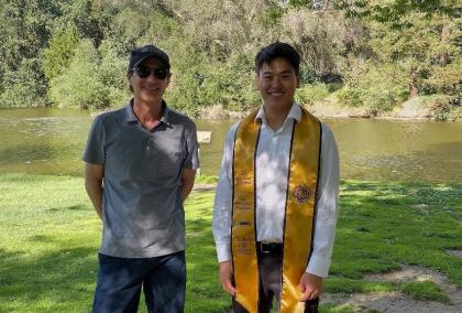 Javier Arévalo with a graduated student standing in front of a lake in a park.