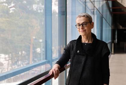 Anita Wagner in front of large windows with trees behind the glass