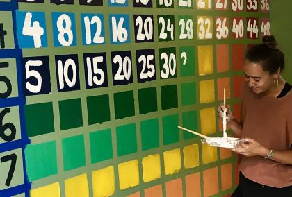 Julia Miller painting a colorful times table on a hall wall.