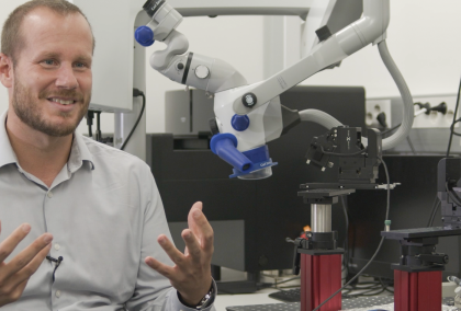 Nelson Totah sitting in front of a microscope in a laboraty. He is looking at the interviewer, explaining something with also using his hands.