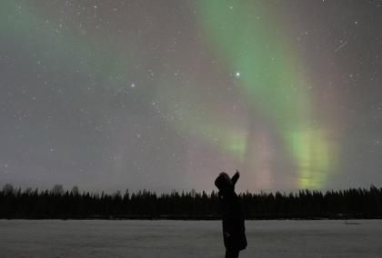 Person pointing Aurora Borealis on the sky during a dark night