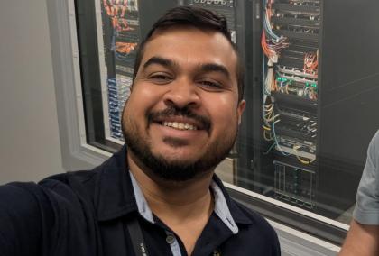 Selfie of Dileepa Marasinghe taken at a lab, with machinery in the background