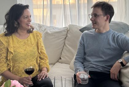 Two people sitting on a white couch talking with each other.