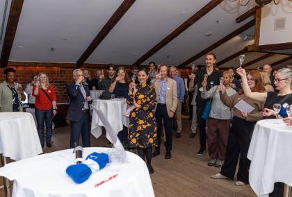 A large group of people smiling and raising a glass in celebration