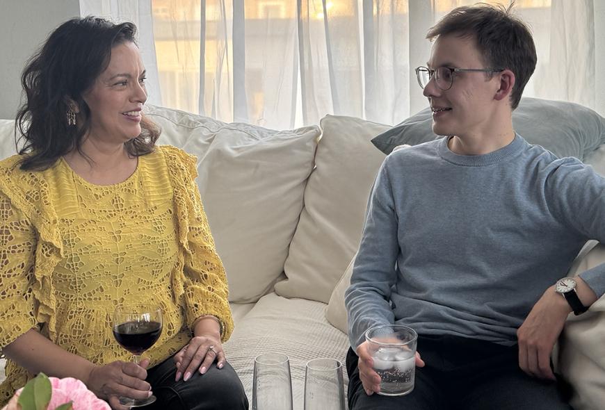 Two people sitting on a white couch talking with each other.