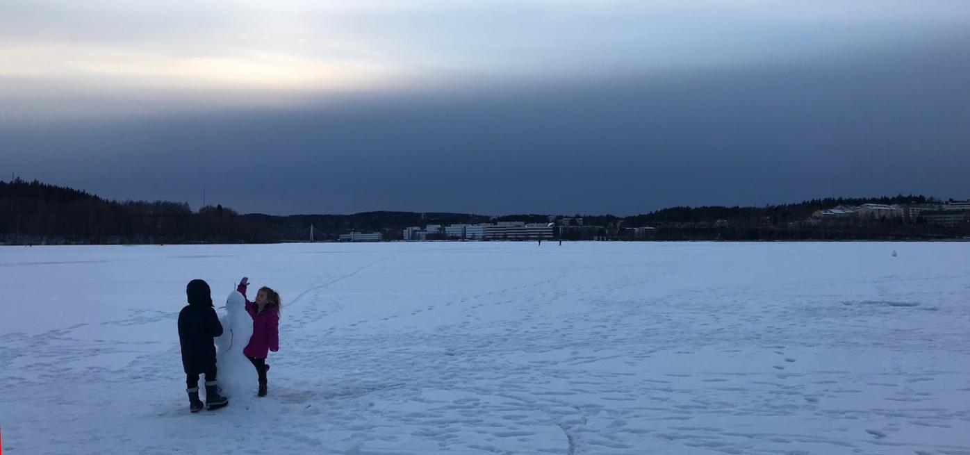 Two children building a snowman on a frozen lake. 