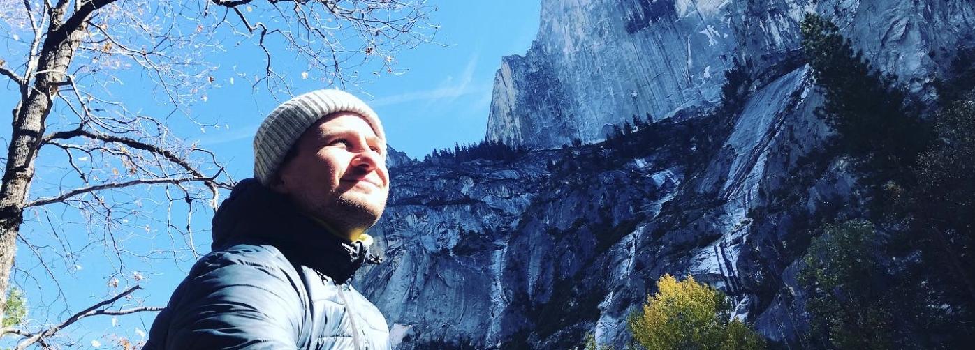 Joonas Lehtovaara at Yosemite, there is a big mountain behind him. Joonas is located on the left side of the photo and he is looking at the direction of sun, his face is lit by it.