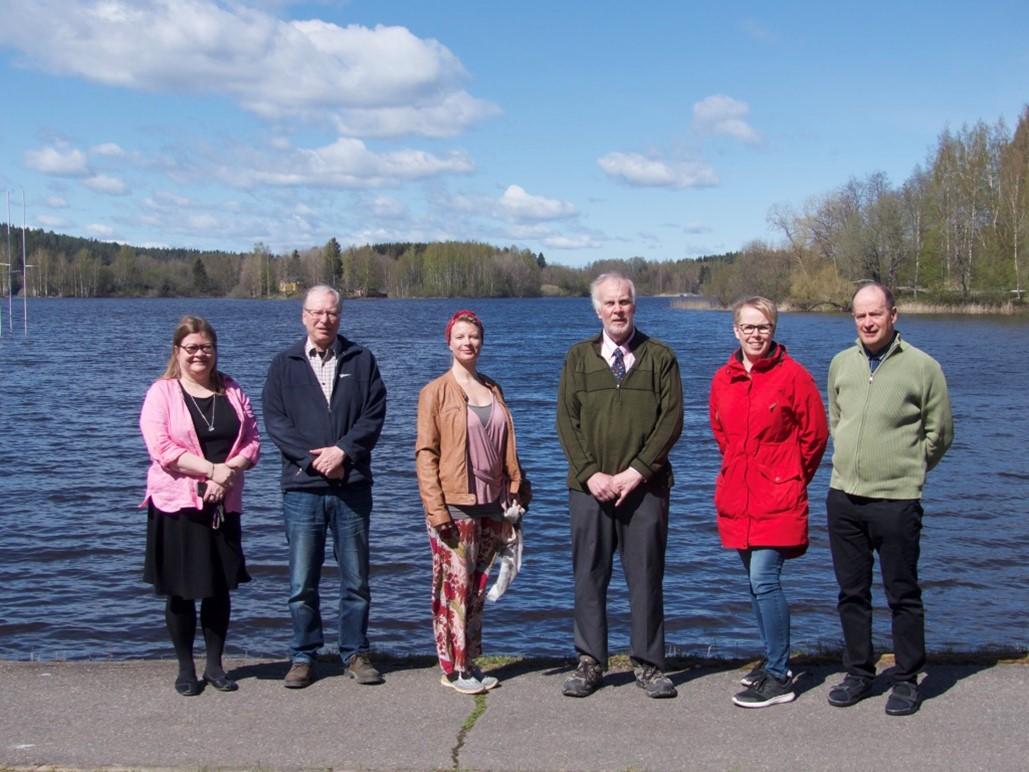 David Dorman with five Finnish colleague photographed in front of a lake on a sunny day.