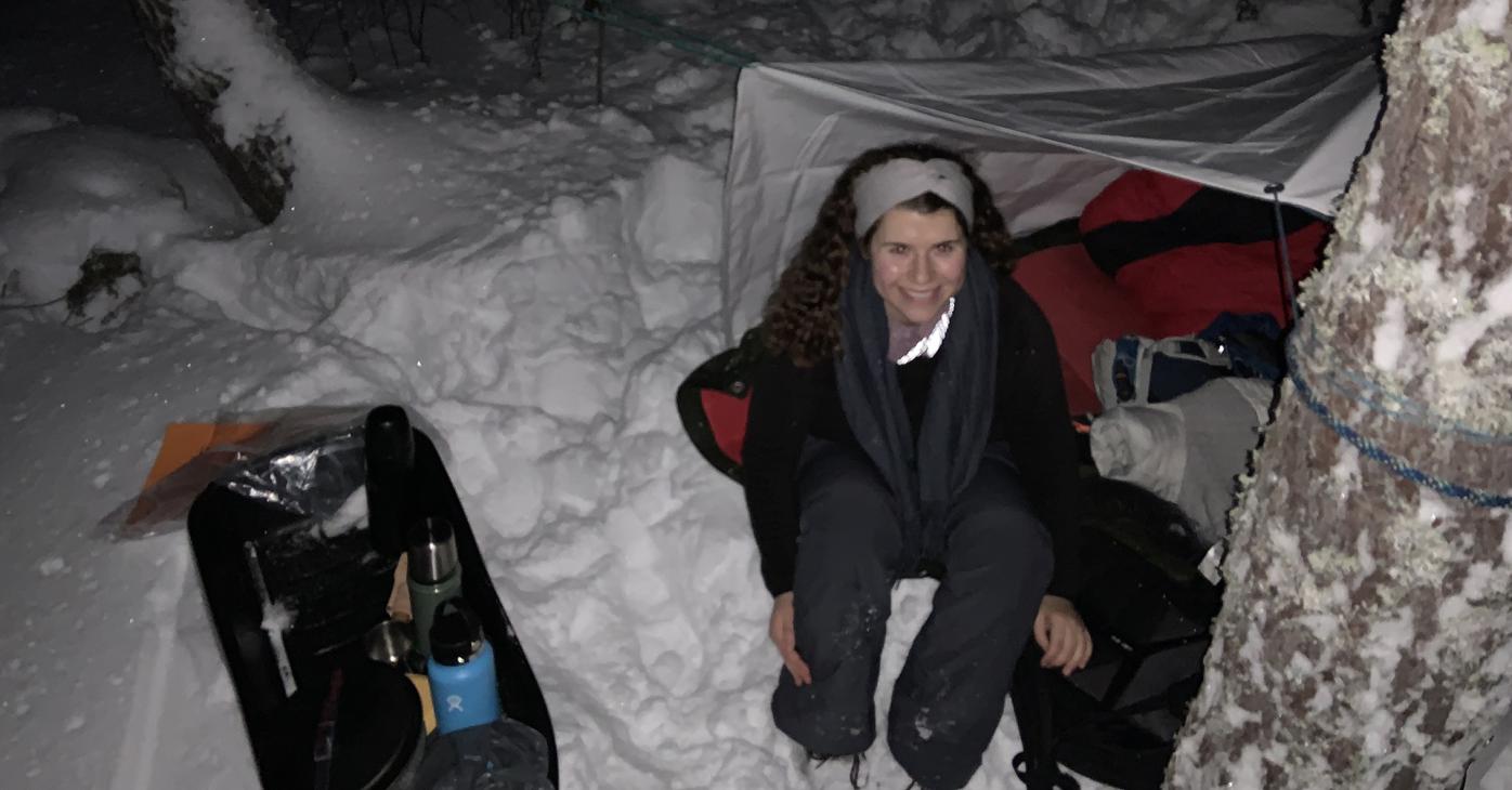 Salena Bantz sitting in front of a tent in a snowy woods