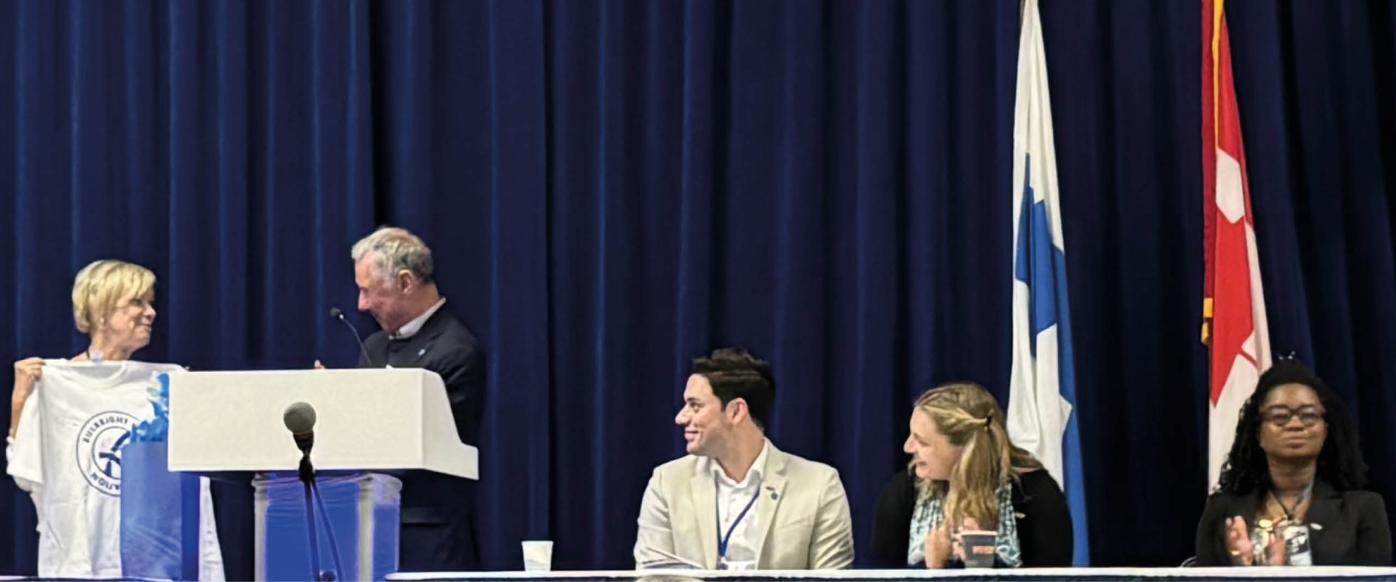 Panel of Fulbright Finland alumni with Ambassador Leena-Kaisa Mikkola. Ed Sivak is handing a white t-shirt with Fulbright Finland Foundation logo on it to the Ambassador.