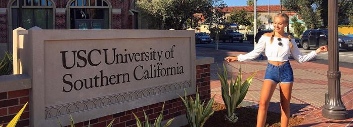 Fulbright Finland Undergraduate grantee Hulda Elopuro next to a USC University of Southern California sign on the university campus. 