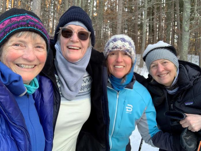 Selife of four women in skiing clothes smiling to the camera. They are in the woods, and have been cross-country skiing in sunny weather.