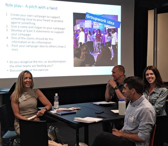 Four Fulbright-Hays fellows around a table, having a conversation while there is a slide with text behind them.