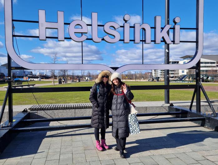 Mikayla Patella-Buckley and her co-teacher in Helsinki, in front of Helsinki sign.