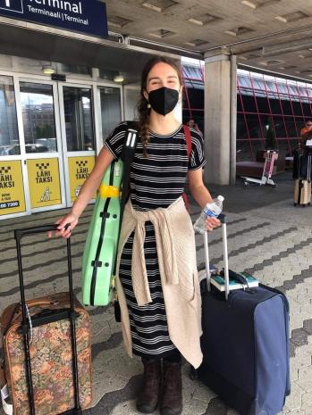 Alyssa with luggage at the airport, just arrived in Finland. She is wearing a mask, but looks happy behind it.