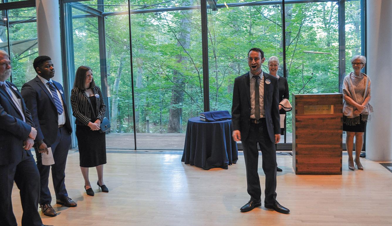 Simon Barrad singing at the Finnish Embassy in Washington D.C. There is a green forest in the background and people listening around Simon