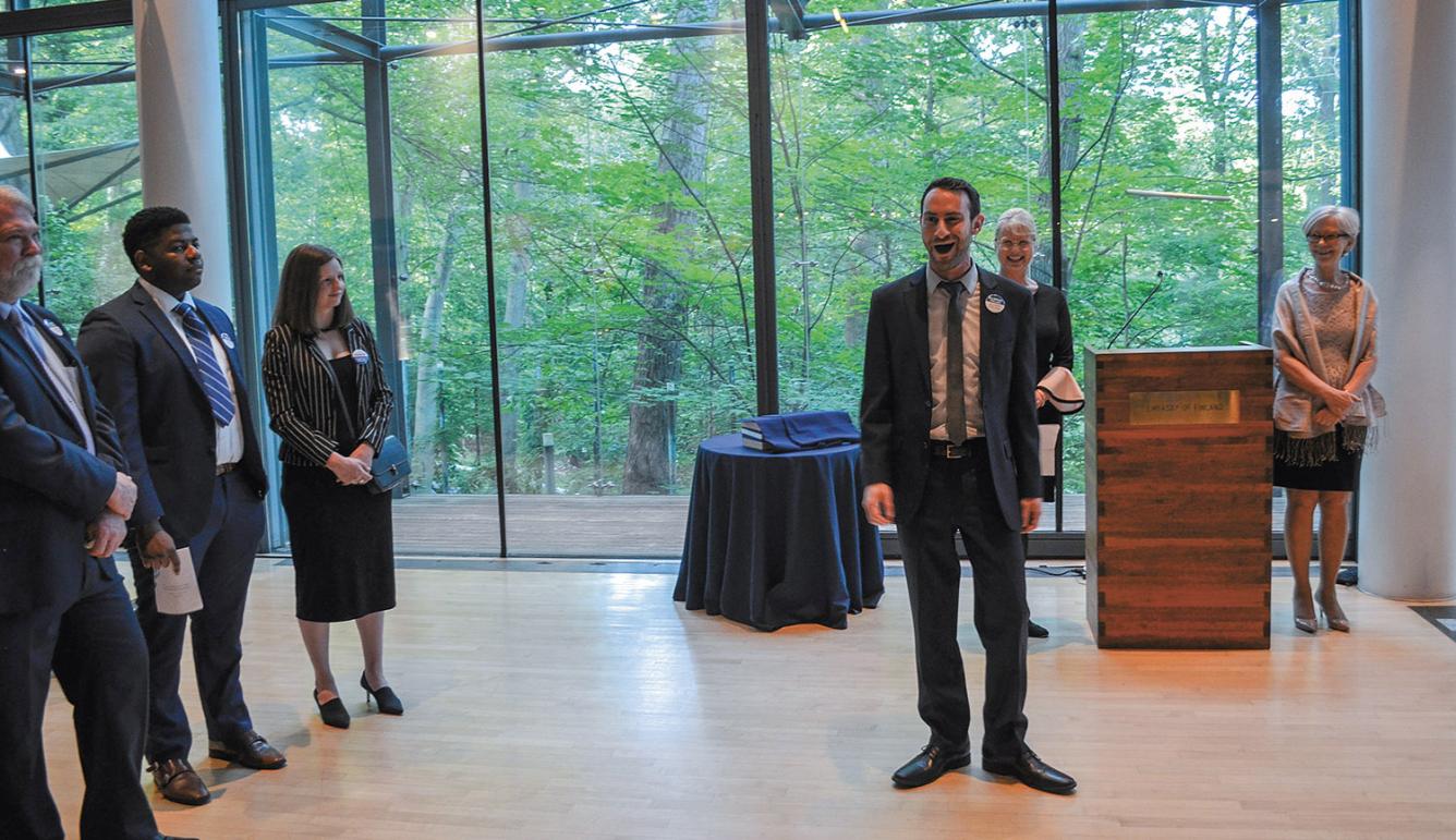 Simon Barrad singing at the Finnish Embassy in Washington D.C. There is a green forest in the background and people listening around Simon