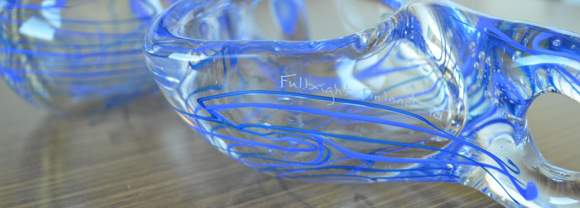 Two blue and white glass Kuksas on a table with "Fulbright Finland 70" carving on them