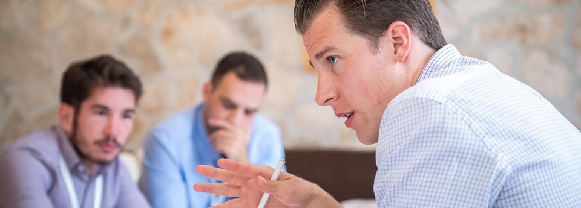 ASLA-Fulbright Graduate alum Miika Tomi talking in a meeting with two men in the background listening carefully