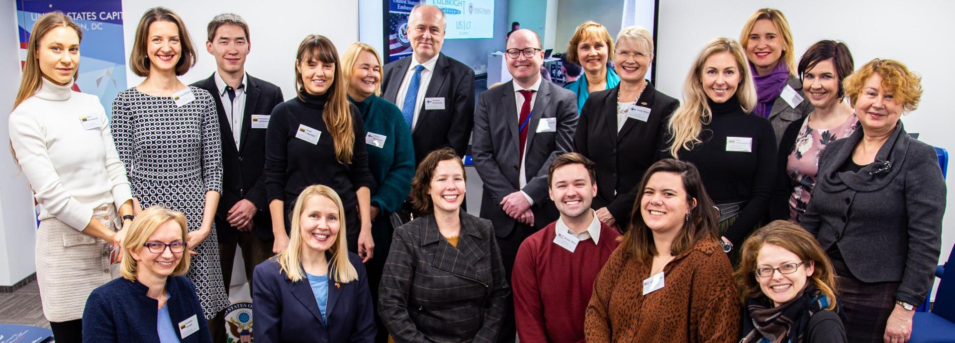 Fulbright Finland alumni and grantees with Lithuanian Fulbrighters at the U.S. Embassy in Vilnius. 19 people in two rows smiling to the camera.