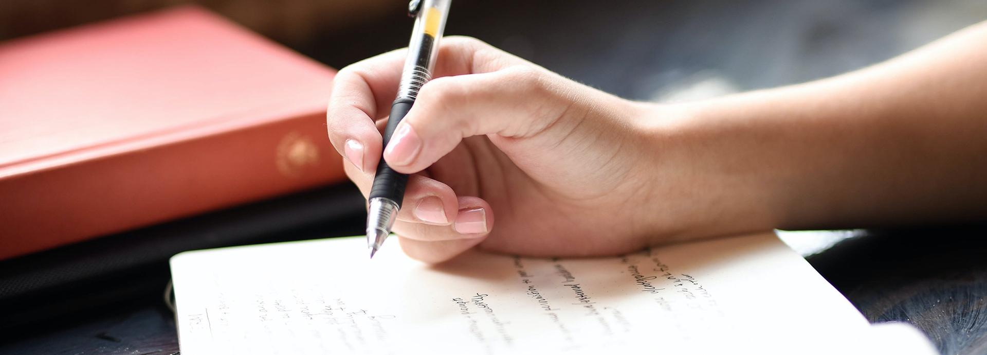 A hand holding a pen over an open notebook on a table