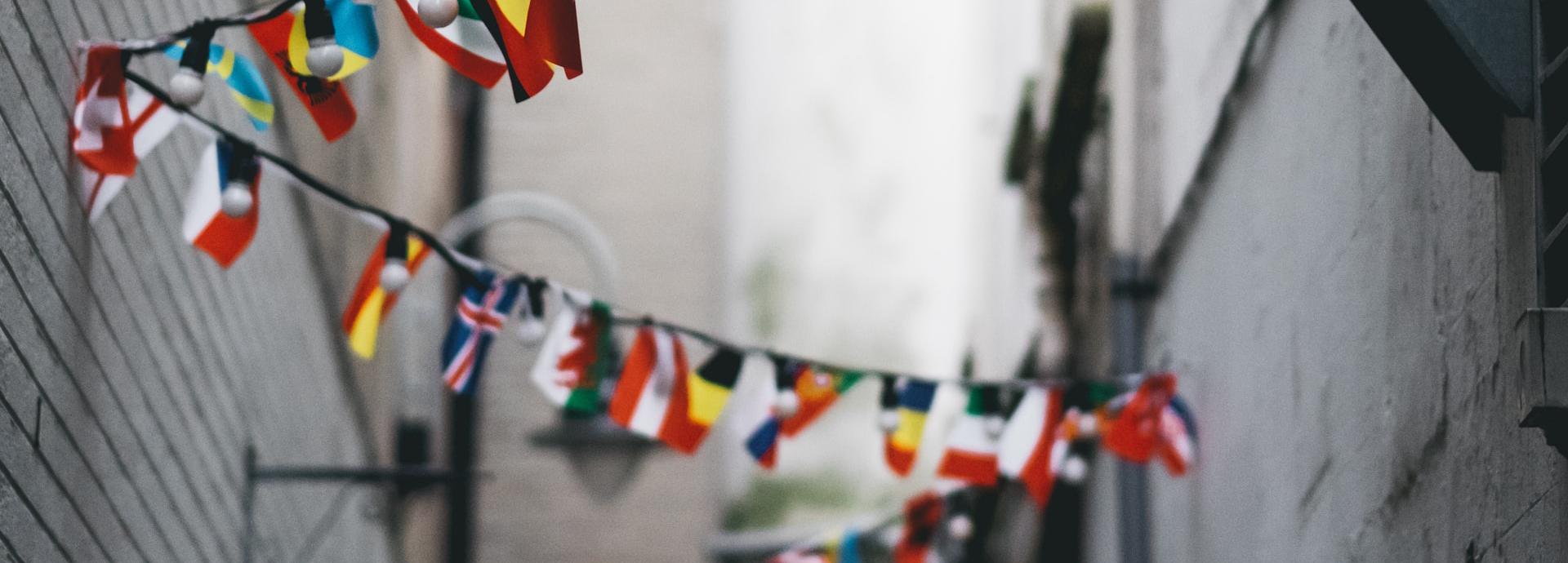 Narrow street with draped flags of different countries and small lights.