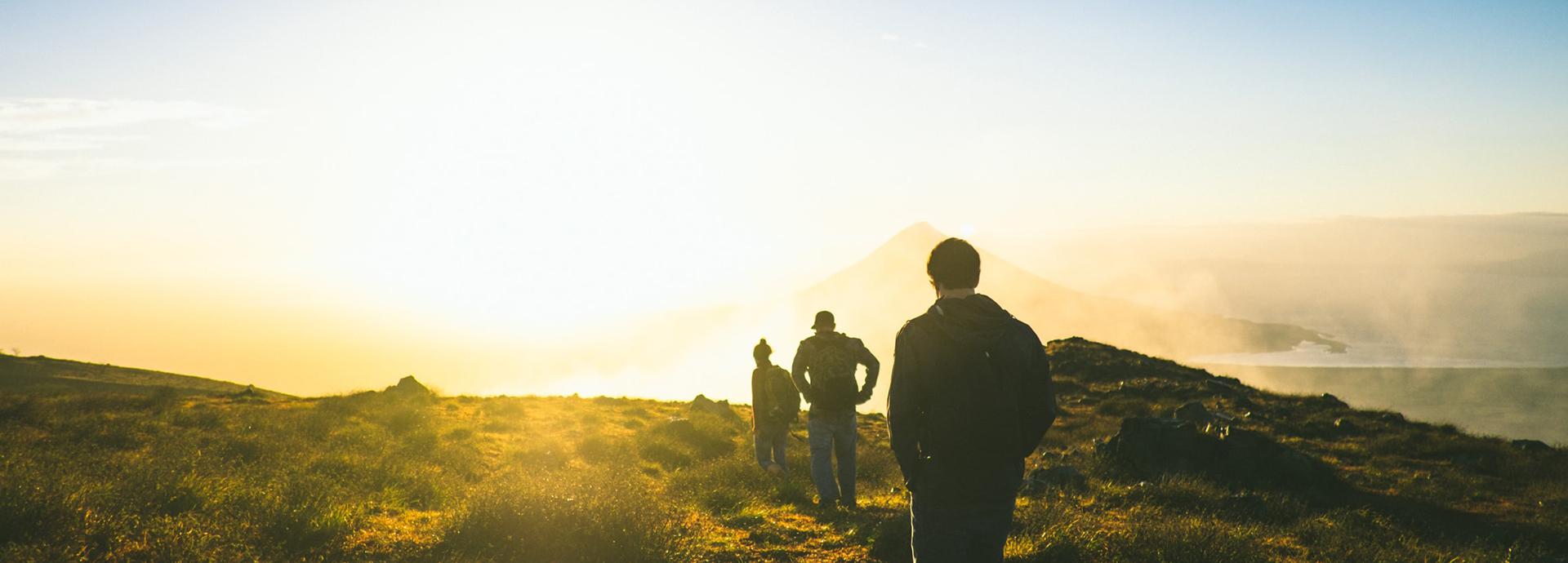 Silhouettes of three people in line when they are walking on a mountain during a golden sunset