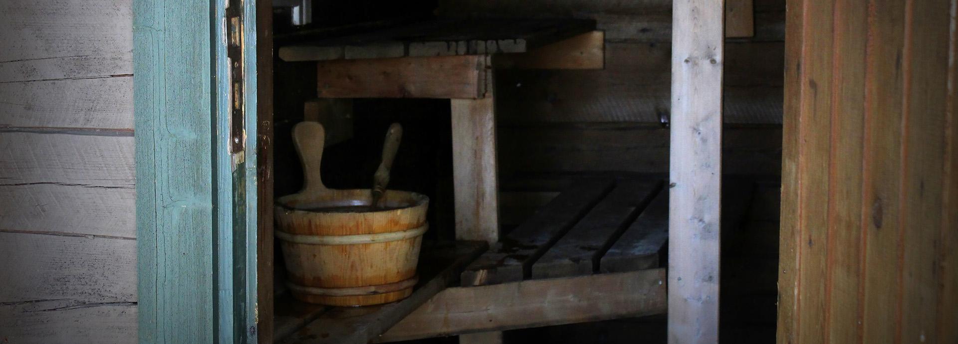 Open door to a sauna, showing a wooden water bucket