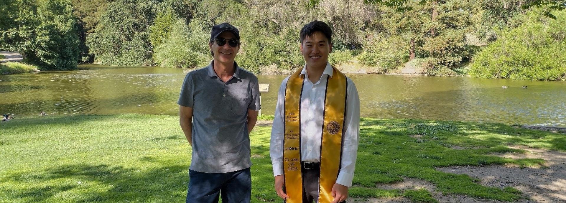 Javier Arévalo with a graduated student standing in front of a lake in a park.
