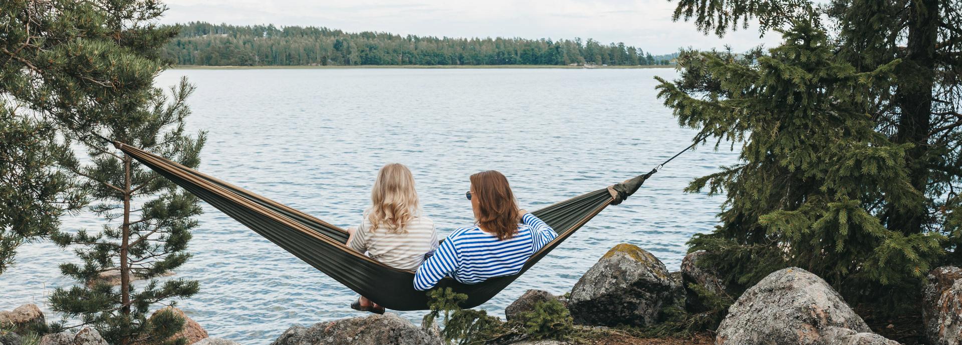 Two people sitting in hammock, looking at lake