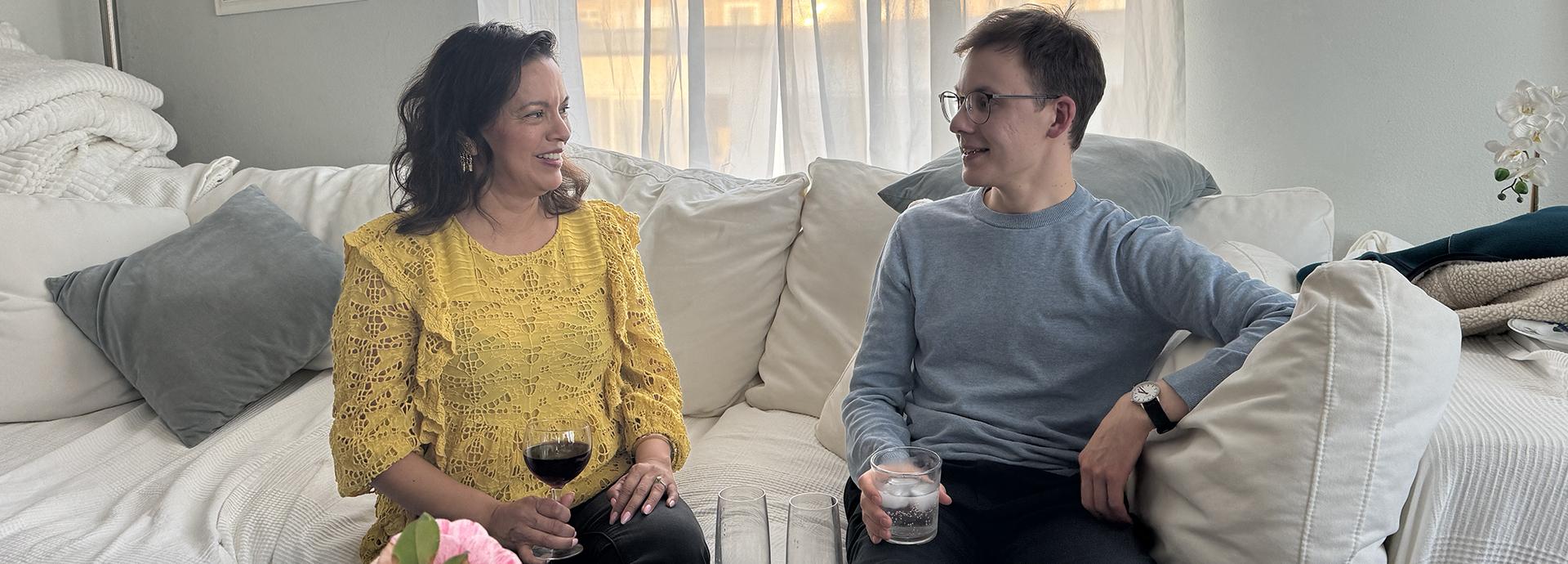 Two people sitting on a white couch talking with each other.