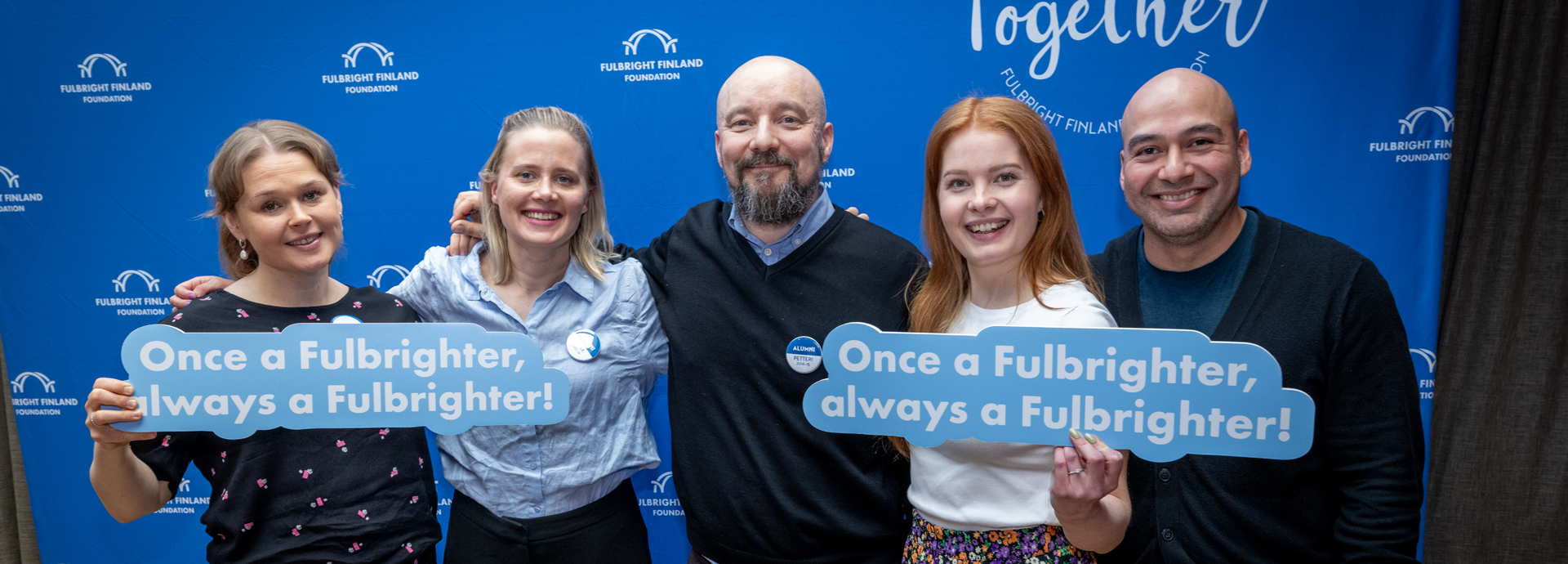 Five Fulbright Finland alumni with "Once a Fulbrighter, always a Fulbrighter!" signs