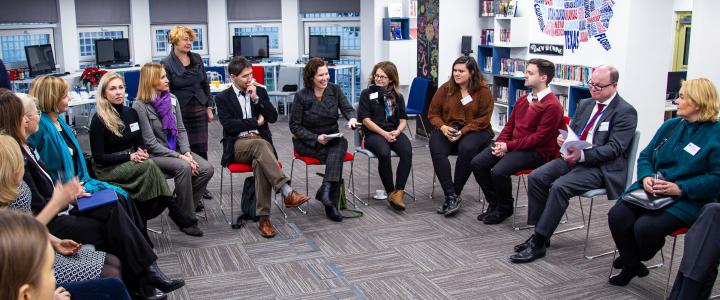 People sitting in a circle. One woman is explaining something with a smile on her face while others are listening to her.