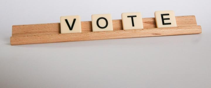 Scrabble tiles spelling out the word VOTE on a wooden Scrabble tile holder