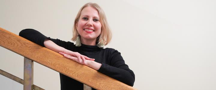 Journalist Kaarina Huovinen slightly leaning on a staircase bannister and smiling to the camera.