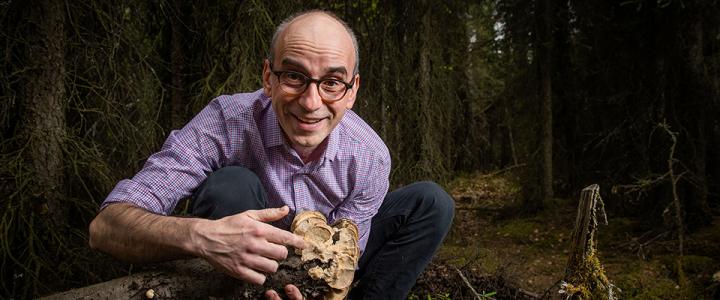 Philippe Amstislavski in a forest, pointing at fungi growing on a tree trunk and smiling at the camera